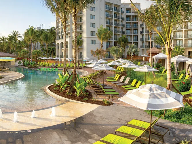 Sunny timeshare in Puerto Rico resort with a pool, lime green loungers, striped umbrellas, palm trees, and a multi-story hotel.