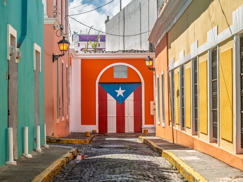 Colorful cobblestone alley in Old San Juan with a Puerto Rican flag painted on an arched door.
