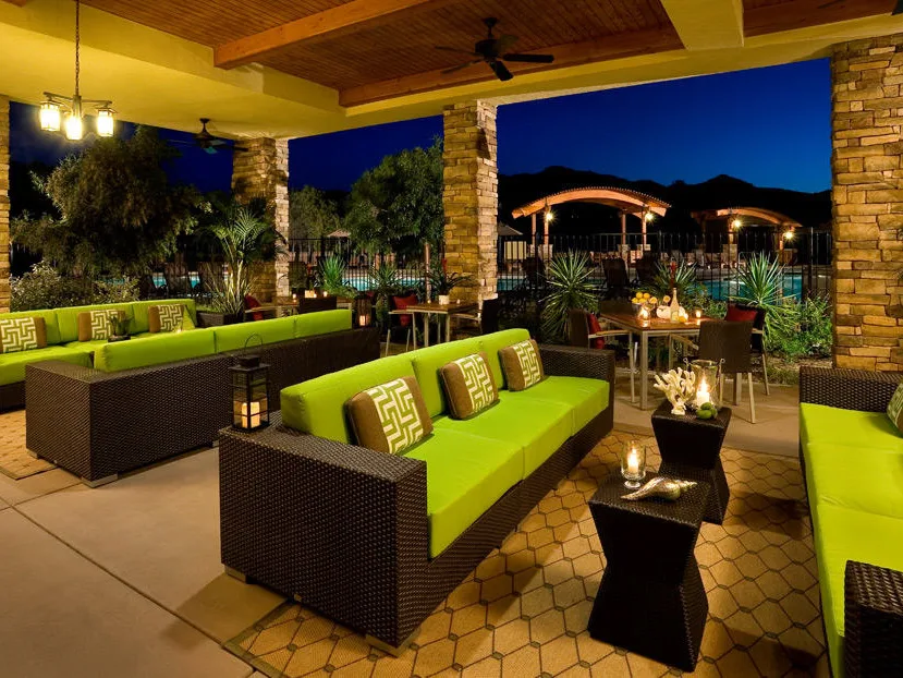 Wicker sofas and green cushions on the patio of a San Diego timeshare, overlooking a glowing pool at dusk.
