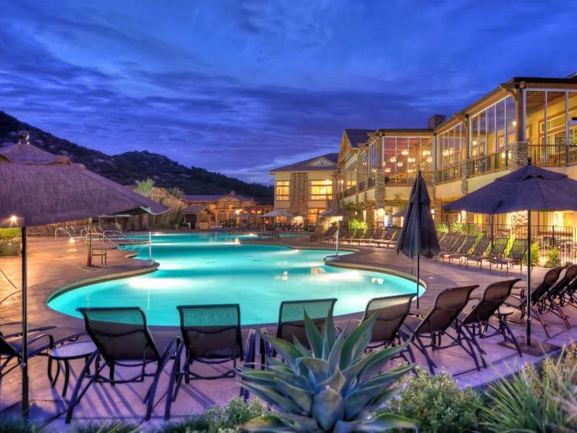 Resort pool glowing at dusk beside a multi-story timeshare in San Diego, with lounge chairs and thatched umbrellas.