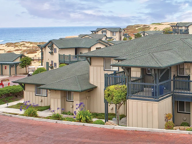 Coastal tan resort buildings with green roofs near sandy dunes and the ocean at WorldMark Marina Dunes.
