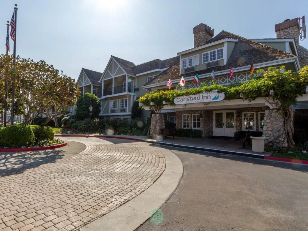 Carlsbad Inn Beach Resort exterior with brick driveway, international flags, and vine-covered entrance in Carlsbad, California.