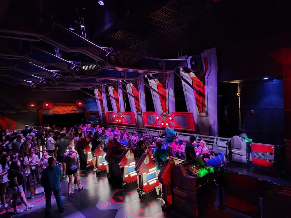Guests board one of the best Epcot rides, a sci-fi indoor coaster with red and purple vehicles in a darkened space-themed area.