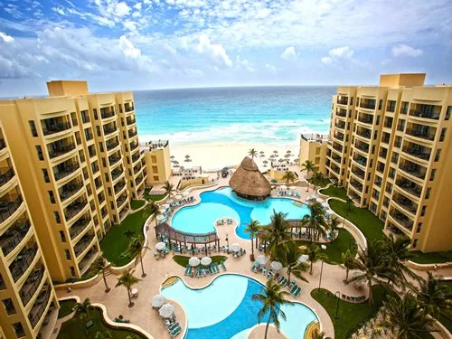 Aerial view of a beachfront resort with a curved pool, palm trees, and turquoise Caribbean water.