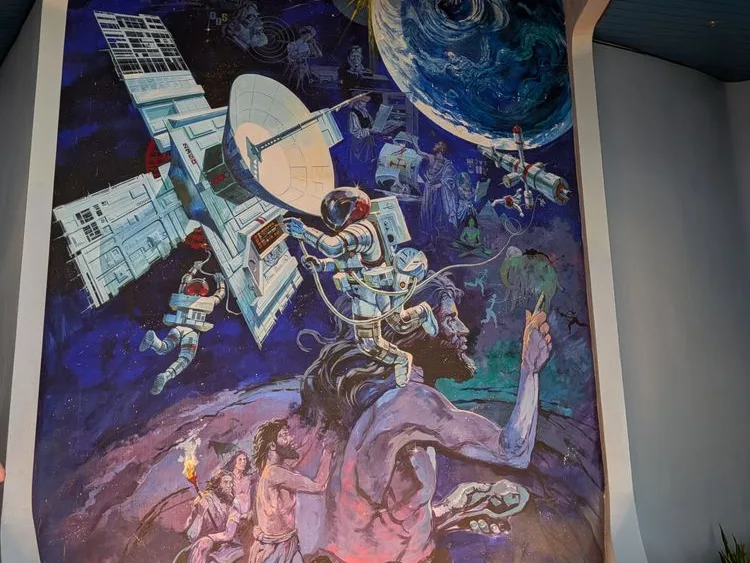 Mural of human evolution seen on one of Epcot rides, from early people with fire to astronauts at a space station.