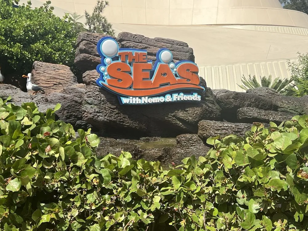 The Seas with Nemo and Friends attraction sign mounted on a rocky facade at EPCOT, surrounded by green hedges.