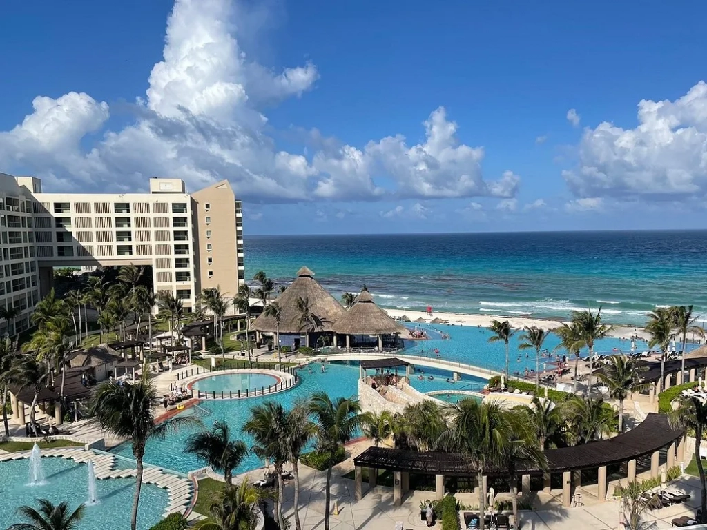 Aerial view of a timeshare in Cancun with turquoise pools, palm trees, and a thatched bar pavilion on the Caribbean coast.